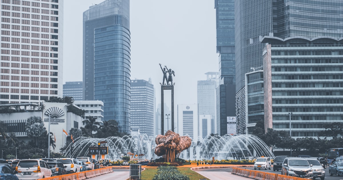 The Selamat Datang Monument and fountain at the Hotel Indonesia Roundabout in central Jakarta, surrounded by traffic and high-rise towers