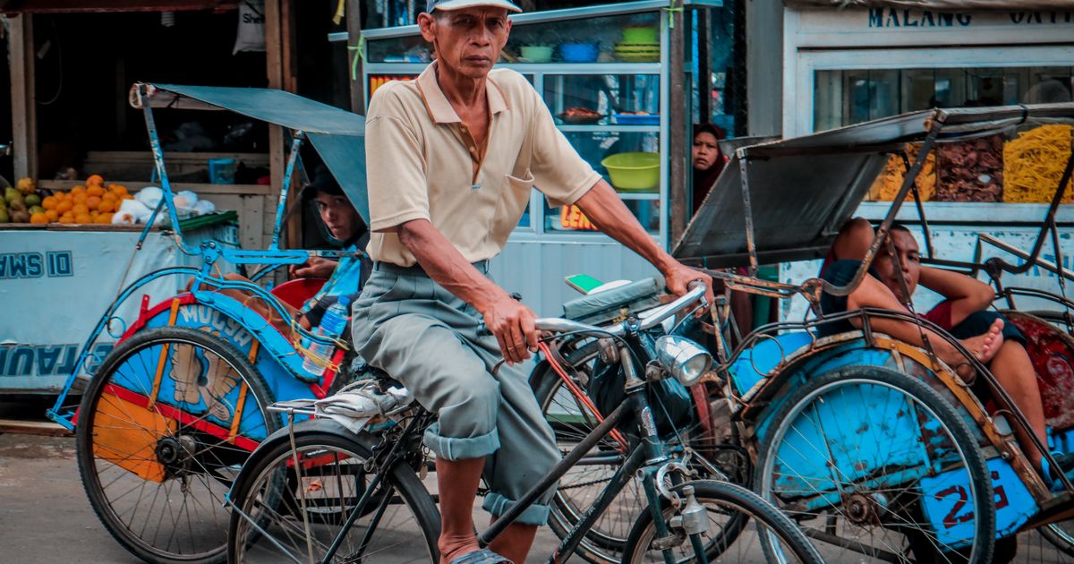 A becak driver waits on his cycle rickshaw in front of food stalls at a traditional Indonesian market